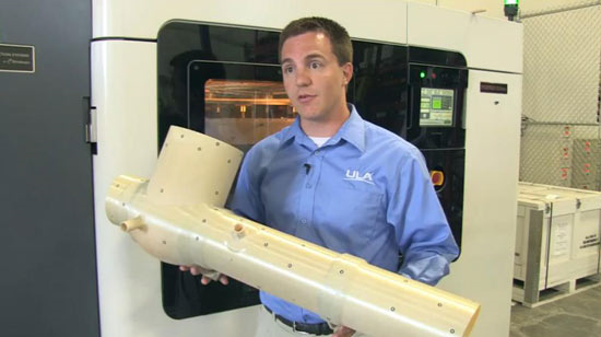 Kyle Whitlow, ULA Structural Engineer, holding the ECS duct produced on the Fortus 900mc 3D Production System (in background)