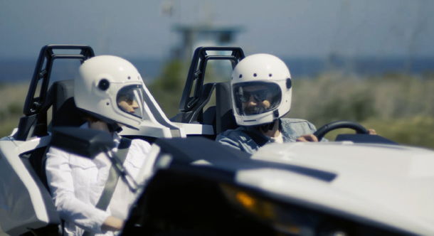 two men talking while driving a sports car